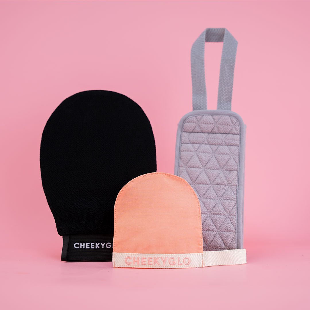 Against a pink background, three exfoliating gloves are showcased: one black labeled "CHEEKYGLO," one peach labeled "CHEEKYGLO," and one gray with a handle, featuring a quilted pattern that makes it ideal for self-care. Elevate your skincare routine with the Cheekybro Set from CheekyGlo&