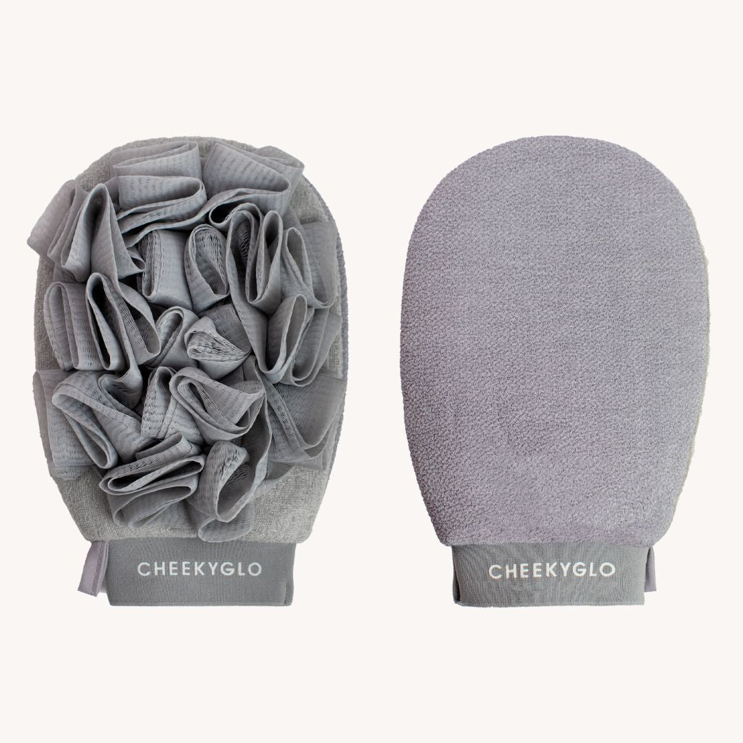 Two CheekyGlo Exfoliating Loofah Gloves are shown. The left glove features textured fabric loops and folds for scrubbing, making it ideal for tackling keratosis pilaris, while the right mitt has a smooth, soft surface for gentle skin smoothing. Both gloves display the word "CHEEKYGLO" at the bottom.