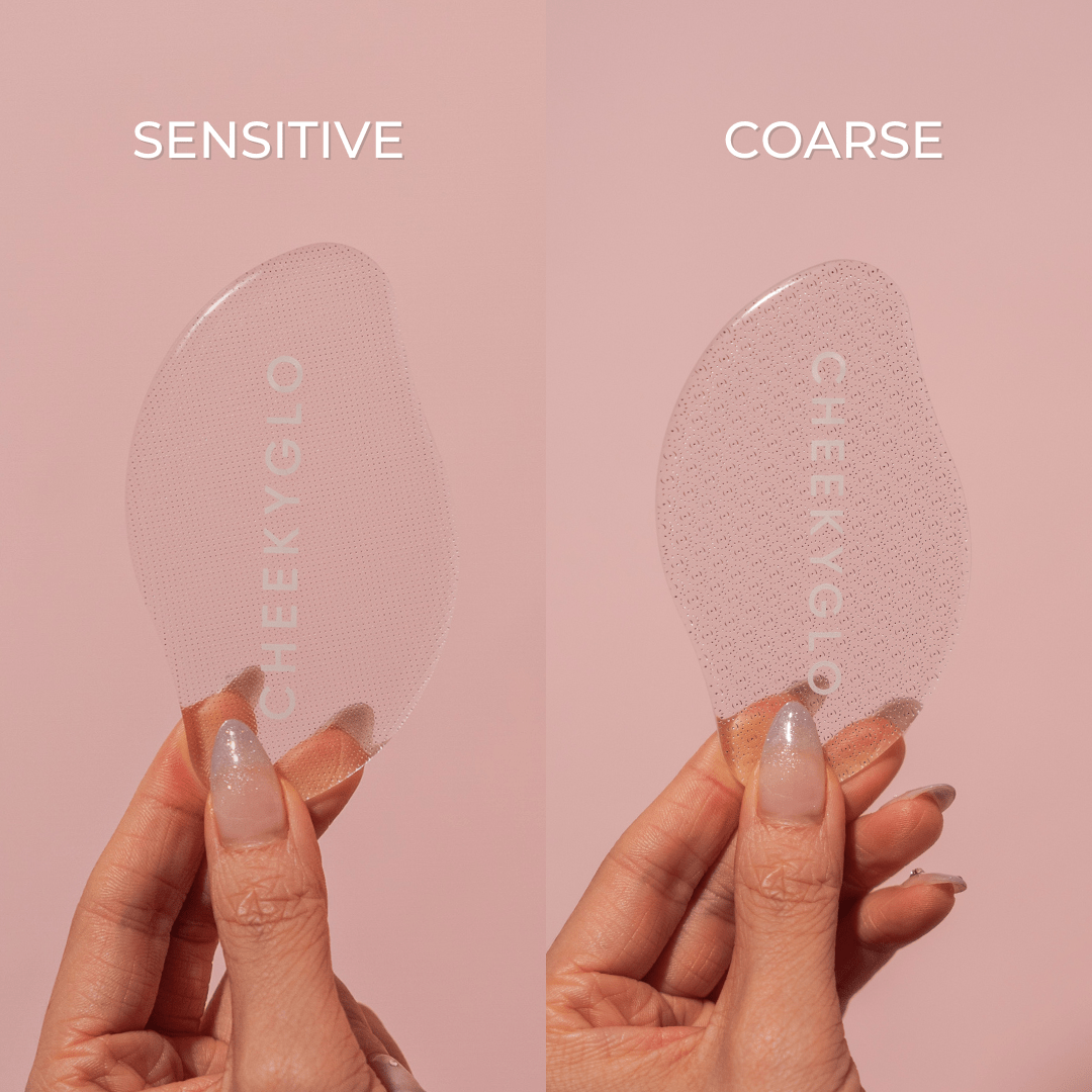 Two hands hold "Sensitive" and "Coarse" exfoliating pads against a pink backdrop. These translucent, textured CheekyGlo pads promise smooth, soft feet through effortless dead skin removal, reflecting the brand&