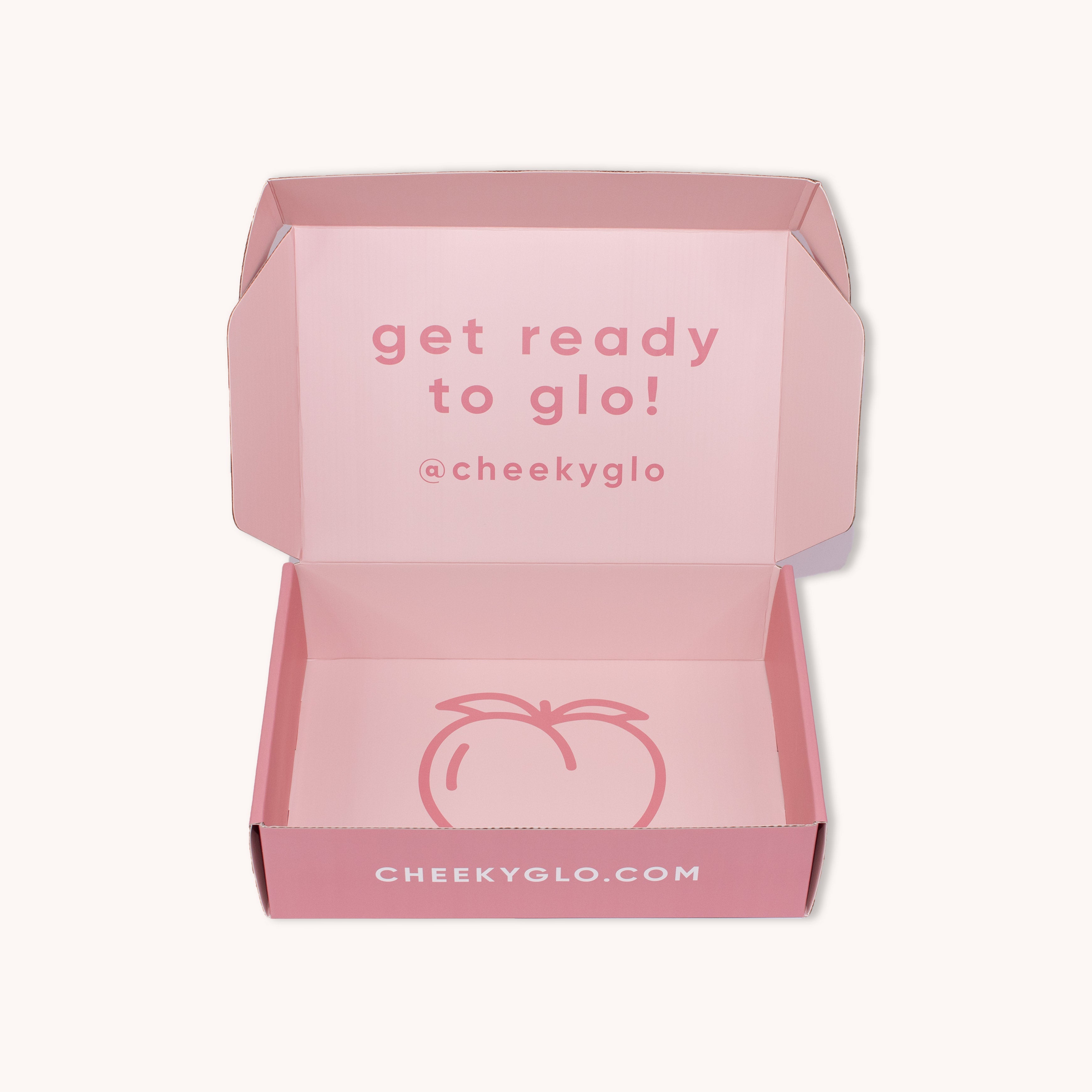 A pink cardboard box with an open lid reveals the inside message "get ready to glo!" and the handle "@cheekyglo". The bottom of the box features a simple peach illustration and the website "CHEEKYGLO.COM", promising a delightful self-care experience with CheekyGlo&