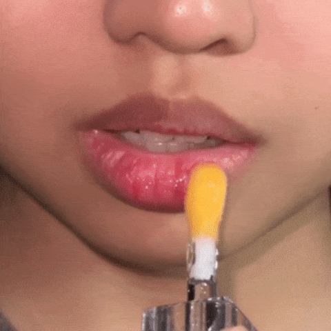 Woman applying the CheekyGlo Colour Changing Lip Oil in the shade Coral on her lips. 