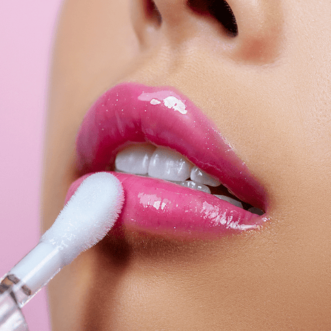 Close-up of a person’s lips being applied with CheekyGlo's Colour Changing Lip Oil using a sponge applicator. The background is a light pink, highlighting the shine and color of the ultra-hydrating formula.