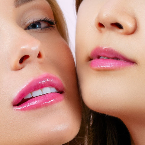 Close-up of two individuals' faces showing glossy pink lips enhanced by CheekyGlo's Colour Changing Lip Oil. The focus is on their lips and part of their noses, highlighting the smooth, flawless skin and subtle makeup. One person has a slightly open mouth, while the other has closed lips.