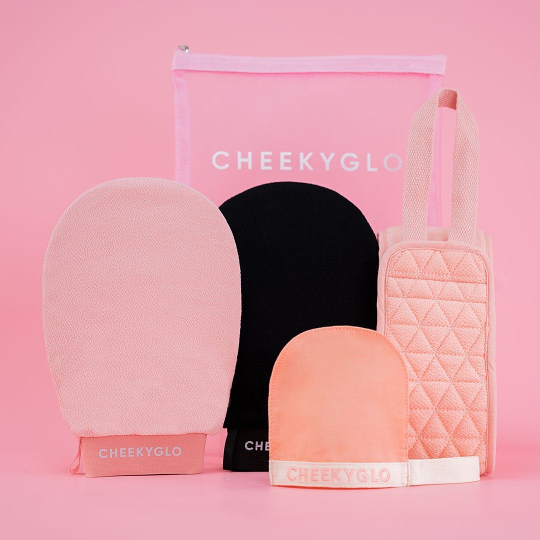 The CheekyGlo Ultimate Glow Set, featuring exfoliating gloves and mitts in pink and black, is elegantly showcased against a pink background. This set is beautifully complemented with a quilted bag and a zippered pouch, perfect for adding style to your skincare routine.