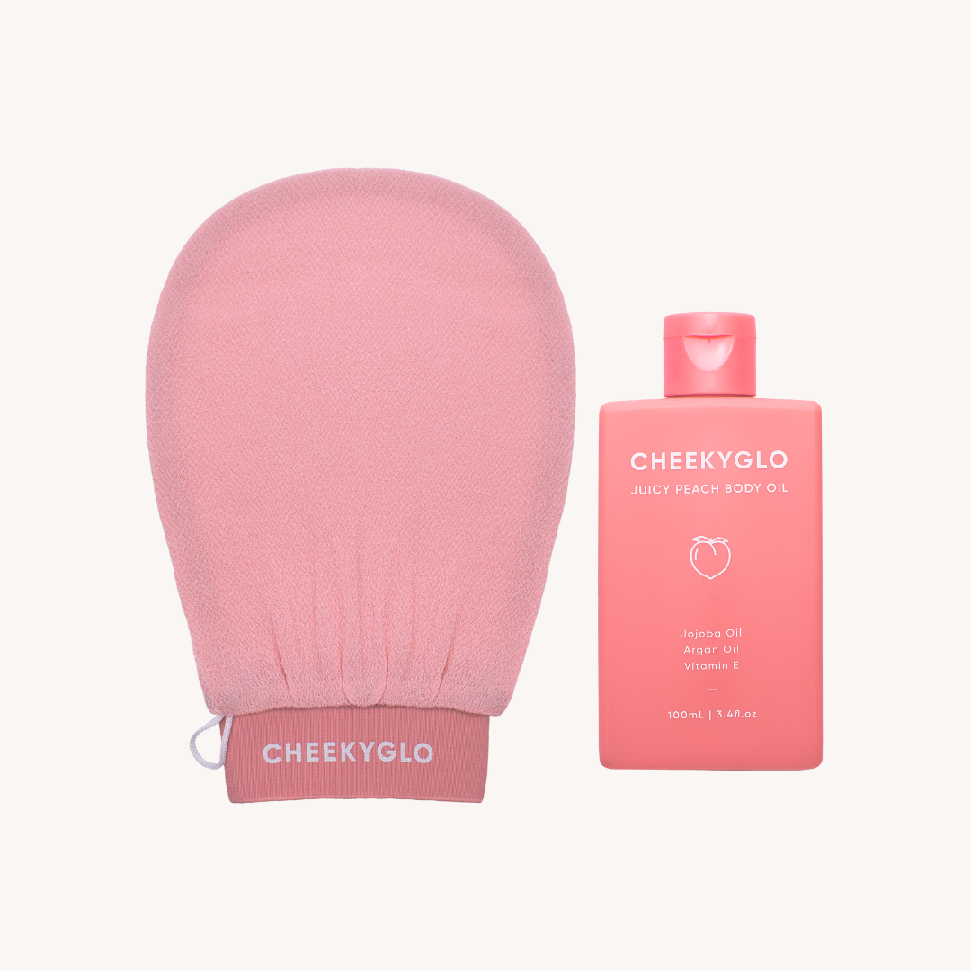 A pink exfoliating glove featuring &quot;CheekyGlo&quot; on the cuff is placed beside a pink bottle of &quot;CheekyGlo Juicy Peach Body Oil.&quot; This body oil, suitable for sensitive skin, includes Jojoba Oil, Argan Oil, and Vitamin E and comes in a 100 ml (3.4 fl. oz) bottle. Both items are part of the popular Glow Up Duo by CheekyGlo.