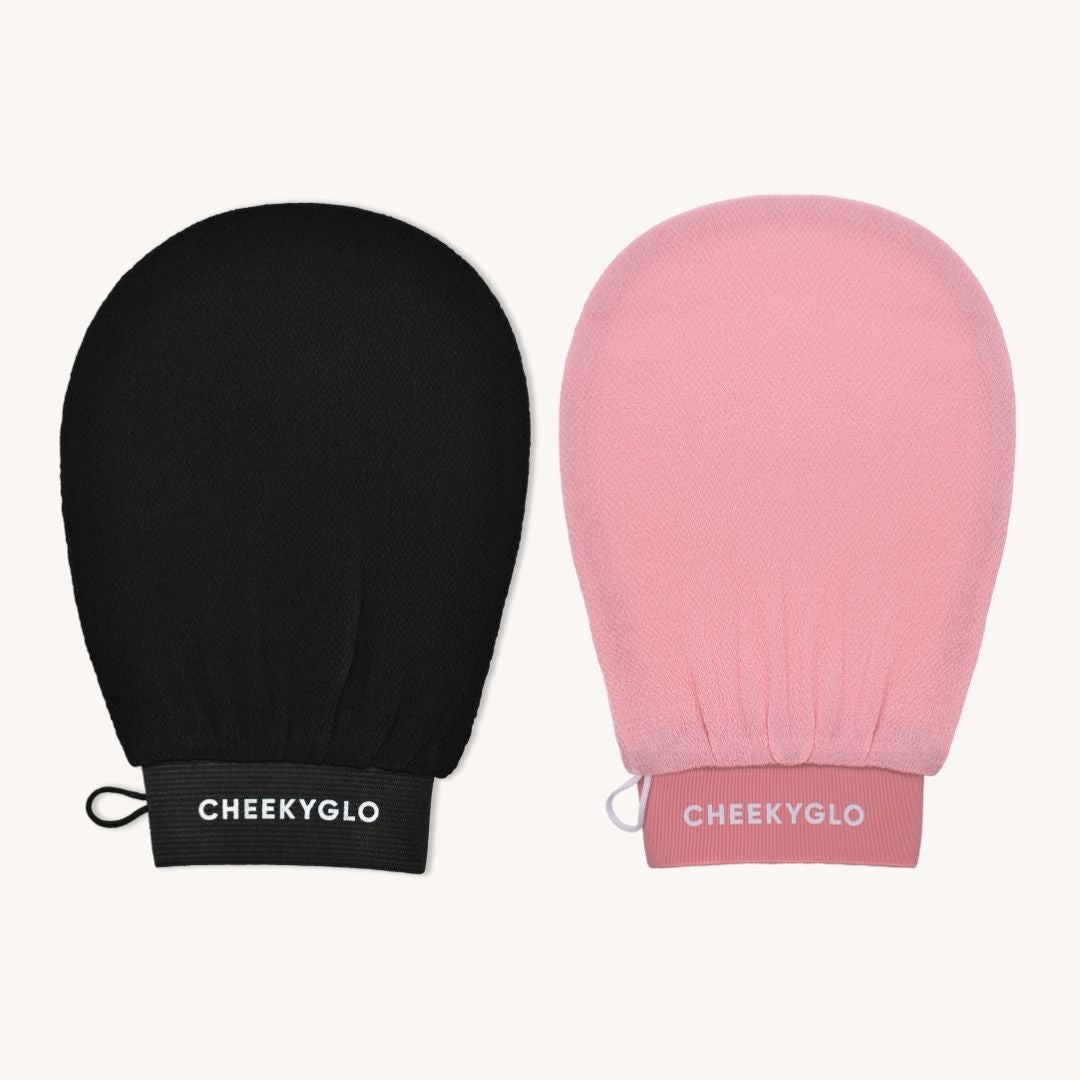 The image showcases the Black+Pink Exfoliating Glove Duo side by side against a plain background. One glove, designed for dead skin removal, is black with &quot;CheekyGlo&quot; printed in white letters, and the other glove is pink with the same branding. Each exfoliating mitt features a small loop for hanging, promising smoother skin.