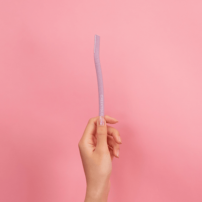 A hand holding a pink CheekyGlo Dermablades facial razor with eco-friendly blades, featuring the brand name &quot;CheekyGlo,&quot; against a pink background.