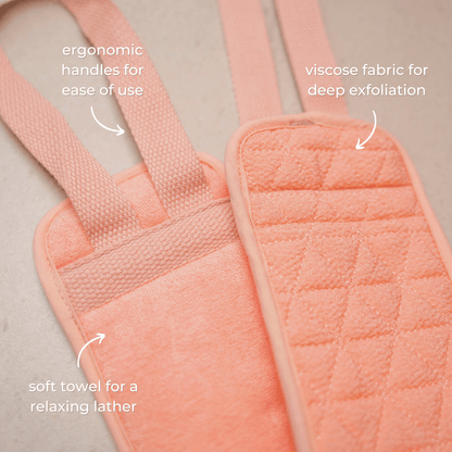 The CheekyGlo Exfoliating Back Scrubber by CheekyGlo is showcased in pink, featuring ergonomic handles. It offers a dual-sided experience: one side for lathering with a soft towel texture, and the other made from biodegradable viscose for deep exfoliation, making it perfect for congested skin. The text highlights its ergonomic handles, viscose material, and soft towel features.