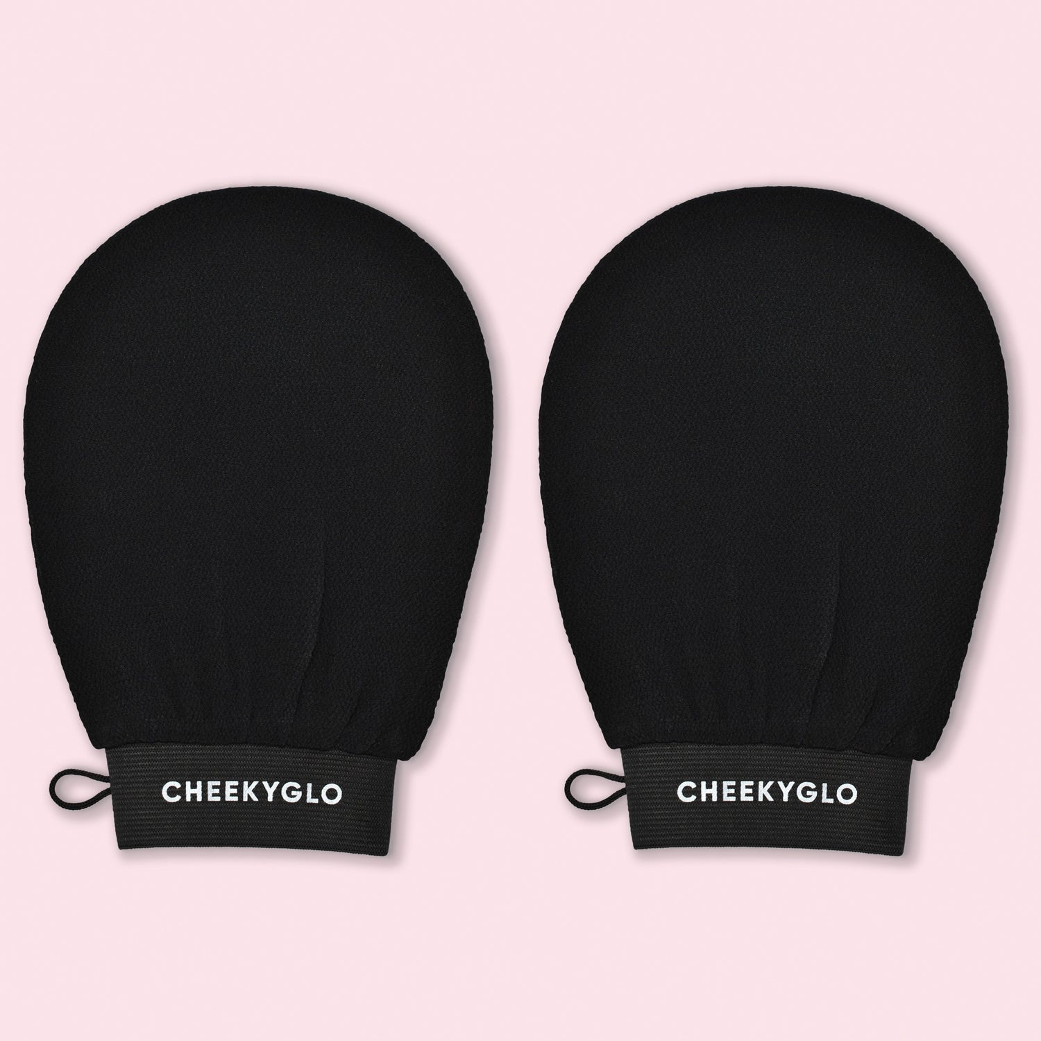 A pair of black exfoliating gloves, known as the &quot;CheekyGlo Exfoliating Glove,&quot; features a textured surface and a loop for hanging. Displayed against a pastel pink background, these gloves are designed to help you achieve smoother skin. The brand name &quot;CheekyGlo&quot; is written in white on the elastic wristbands.