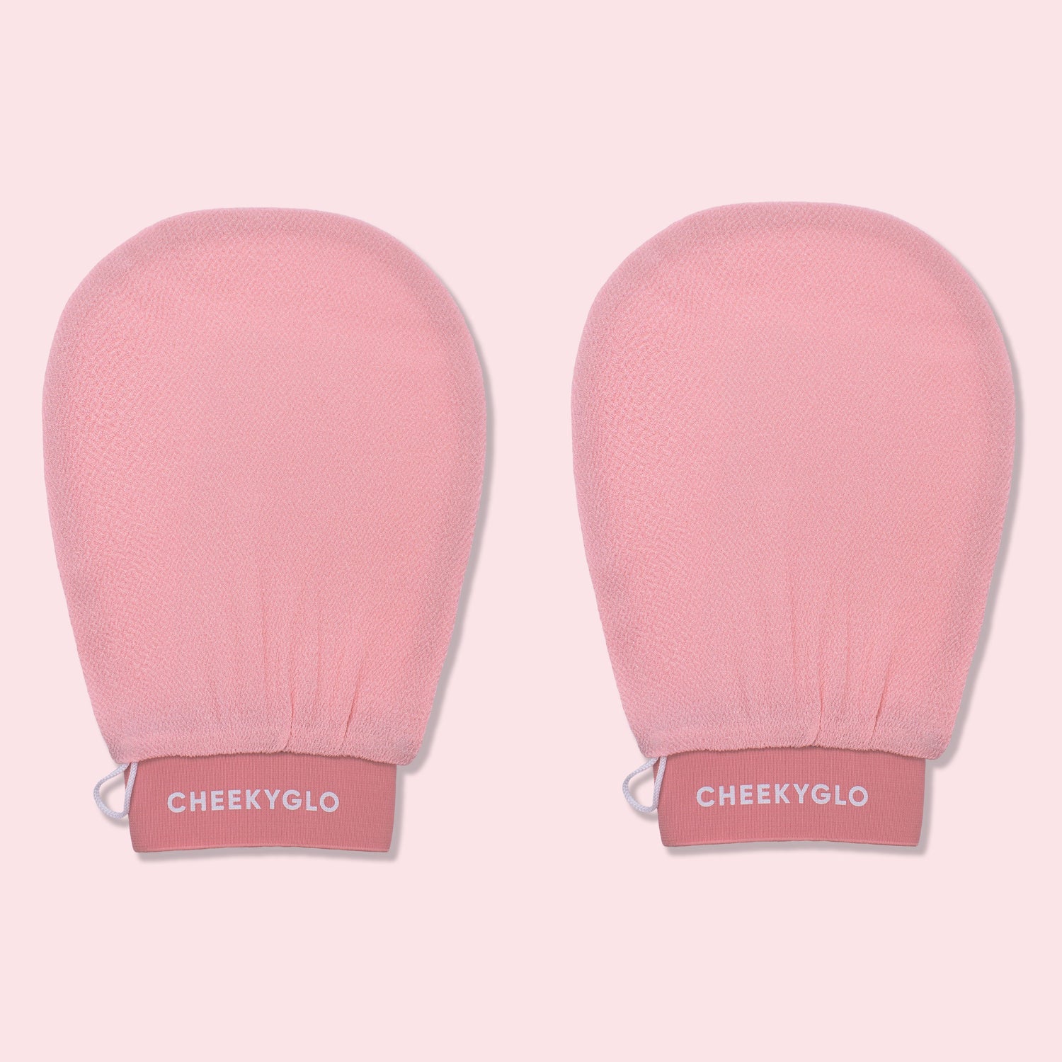 Two pink CheekyGlo Exfoliating Gloves with &quot;CheekyGlo&quot; printed in white on the wristbands. The gloves promise smoother, healthier skin and are set against a light pink background.