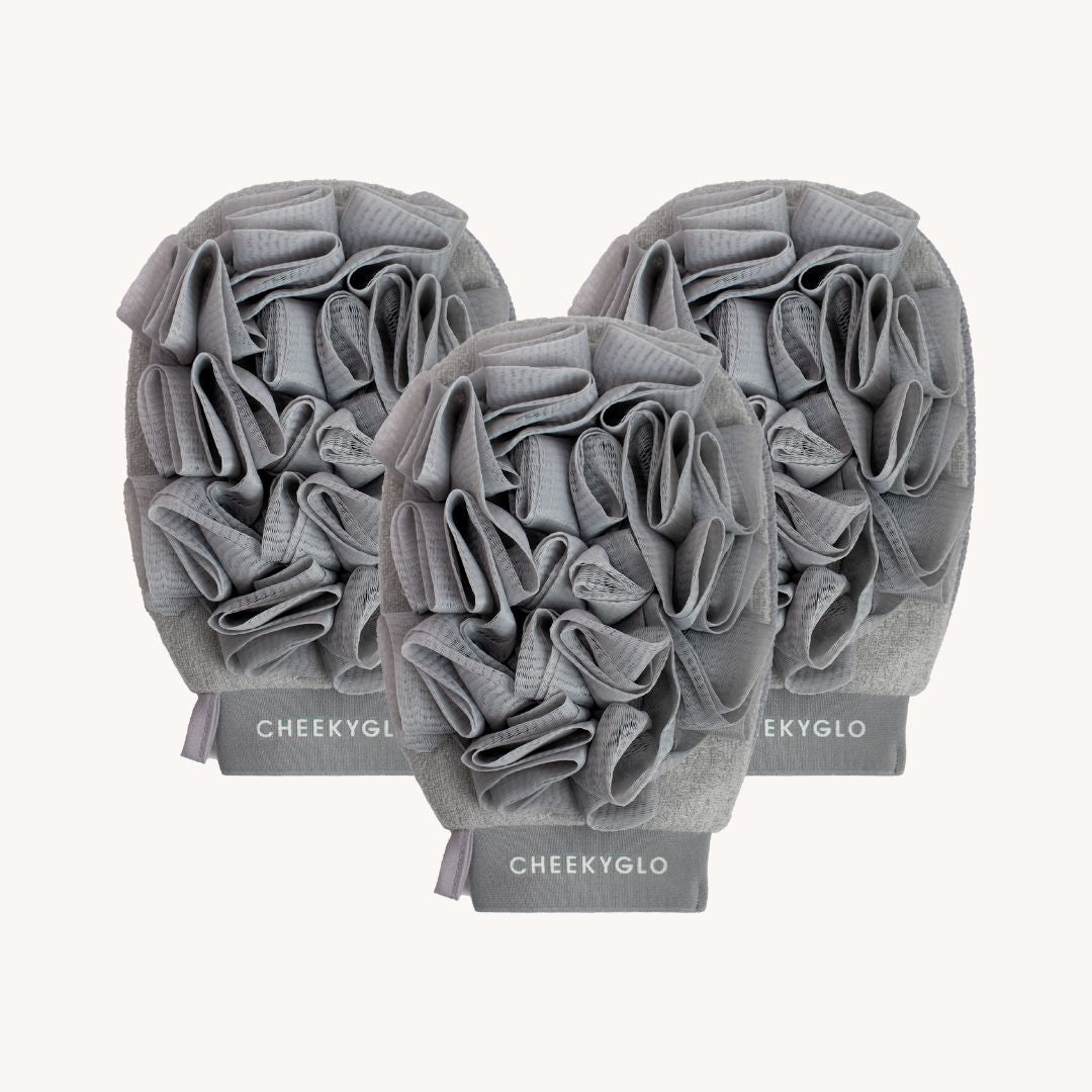 Three grey CheekyGlo Exfoliating Loofah Gloves with textured surfaces are displayed, perfect for skin smoothing and combating keratosis pilaris. The brand name &quot;CheekyGlo&quot; is printed in white on the cuff of each glove. The gloves are arranged in a staggered formation against a light background.