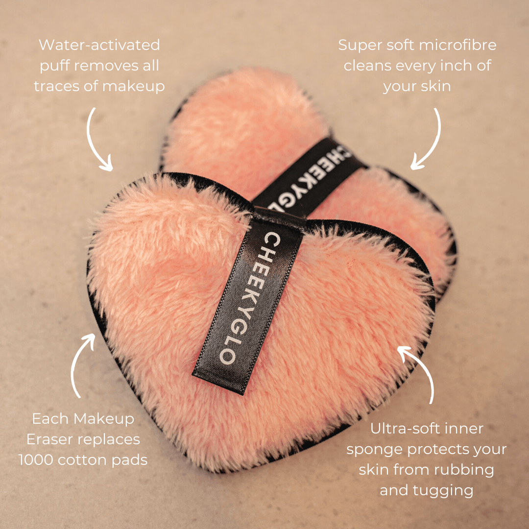 Two heart-shaped pink CheekyGlo Makeup Erasers feature black trim and a looped tag with the brand name &quot;CheekyGlo.&quot; The image showcases their water-activated ability to remove makeup, super soft microfiber exterior, ultra-soft inner sponge, and eco-friendly alternative to cotton pads.