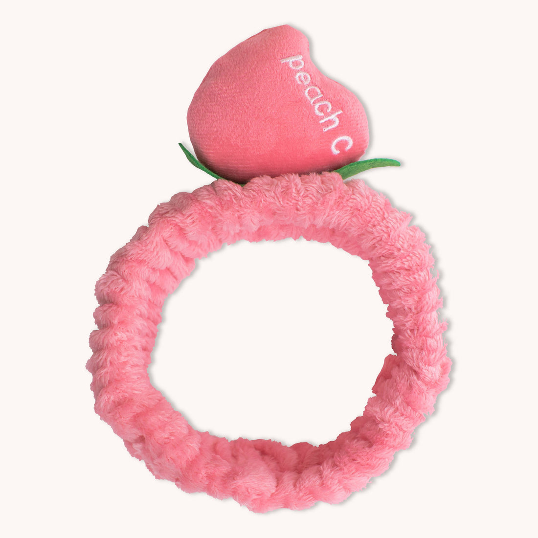 Introducing the CheekyGlo Peachy Headband by CheekyGlo: a pink plush scrunchie featuring a decorative peach on top with &quot;peachc&quot; embroidered in white text. This fluffy elastic headband elevates your self-care routine, providing both style and comfort with its soft and fluffy material.