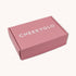 A neatly sealed, closed pink cardboard box with the brand name "CheekyGlo" printed in large white letters on the top surface. This CheekyGlo Premium Gift Box is set against a plain, light-colored background and is perfect for holding precious self-care products or including a special note for someone dear.