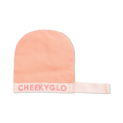 The CheekyGlo Silk Exfoliating Face Mitt, crafted from Premium Turkish Silk in a delicate peach hue, features the word &quot;CHEEKYGLO&quot; embroidered in pink thread on the cuff and is showcased against a black background. This luxurious face mitt from CheekyGlo effectively exfoliates the skin to reveal a radiant glow.