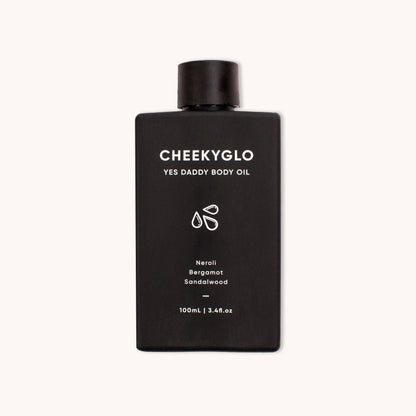 A black bottle of CheekyGlo Yes Daddy Body Oil featuring white text, indicating it is 100ml (3.41 fl oz) and contains ultra-hydrating certified organic ingredients. It boasts scents like neroli, bergamot, and sandalwood. The bottle showcases a minimalist design with subtle droplet graphics.