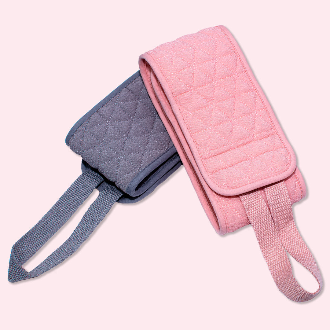 Two CheekyGlo Exfoliating Back Scrubbers, one in pink and the other in blue, are neatly folded with matching straps extended. Crafted from biodegradable viscose, these scrubbers are displayed on a light background, showcasing their soft texture and diamond pattern stitching.