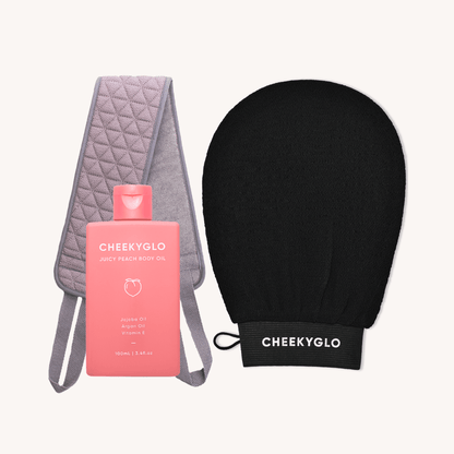 A product bundle called &quot;Fake Tan Set&quot; from CheekyGlo features a pink bottle of Juicy Peach Body Oil, alongside a quilted gray exfoliating strap and a black exfoliating glove. These tools are perfect for moisturizing and exfoliating your skin, making them ideal for prepping before applying your favorite fake tan.