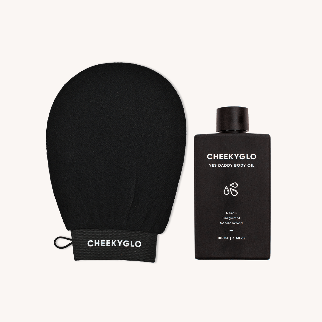 A black exfoliating glove labeled &quot;CheekyGlo&quot; rests beside a sleek bottle of &quot;Glow Up Duo [MOST POPULAR]&quot; body oil from CheekyGlo. This 100ml (3.4 fl oz) gem, ideal for sensitive skin, is infused with Neroli, Bergamot, and Sandalwood oils.