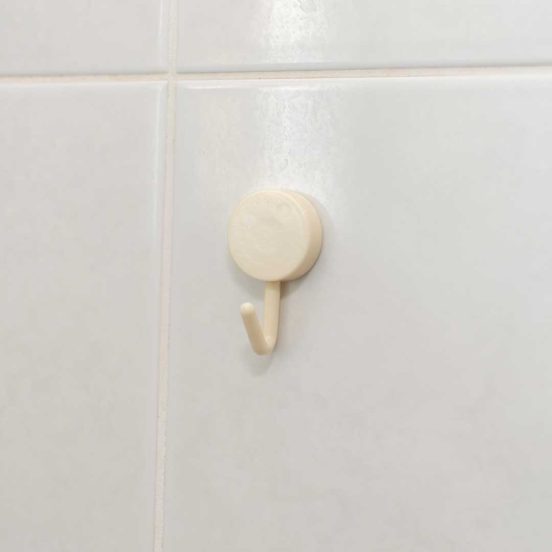 A CheekyGlo Hanging Hook in beige, featuring a simple round plastic design and rust-proof material, is mounted on a white-tiled wall. It appears well-suited for hanging lightweight items.