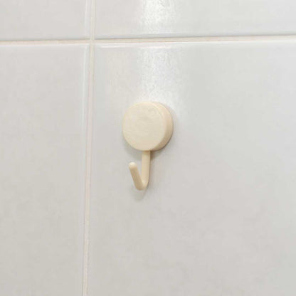 A CheekyGlo Hanging Hook in beige, featuring a simple round plastic design and rust-proof material, is mounted on a white-tiled wall. It appears well-suited for hanging lightweight items.